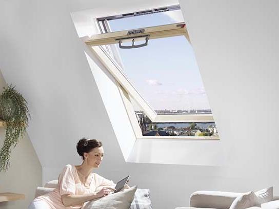 Eine Frau sitzt im Wonzimmer unter einem RotoQ Schwingfenster und hält ein Tablet